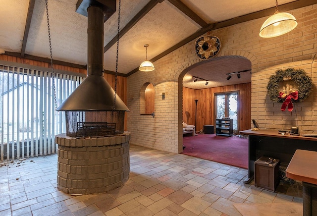 interior space featuring vaulted ceiling with beams, brick wall, a textured ceiling, and a wealth of natural light