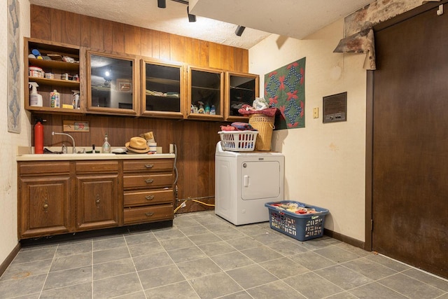 clothes washing area with washer / dryer, laundry area, wooden walls, a textured ceiling, and a sink