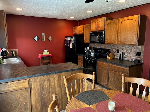 kitchen featuring dark countertops, a peninsula, a textured ceiling, black appliances, and a sink