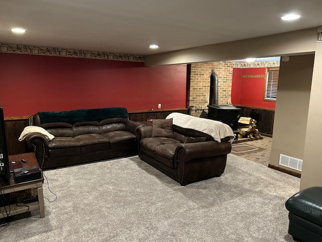 carpeted cinema room with recessed lighting, a wood stove, visible vents, and a wainscoted wall