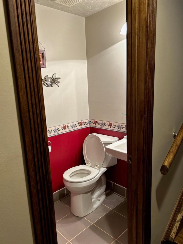 bathroom featuring toilet, tile patterned flooring, and a textured ceiling