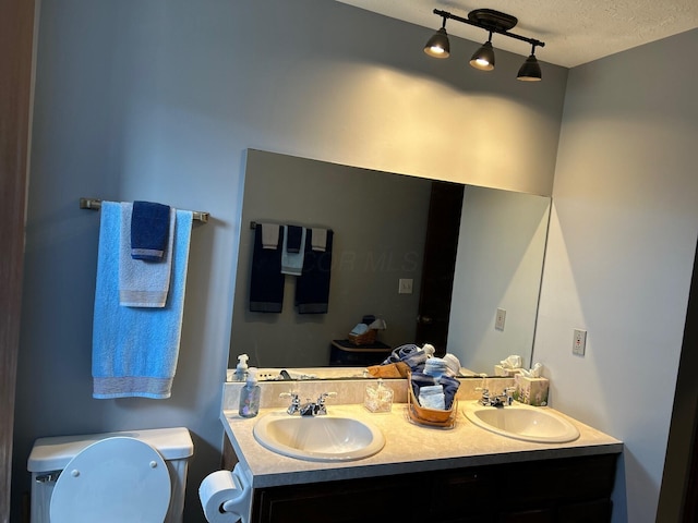 bathroom featuring a sink, a textured ceiling, toilet, and double vanity