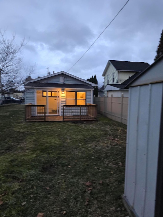 rear view of property featuring a yard, fence, a wooden deck, and an outdoor structure