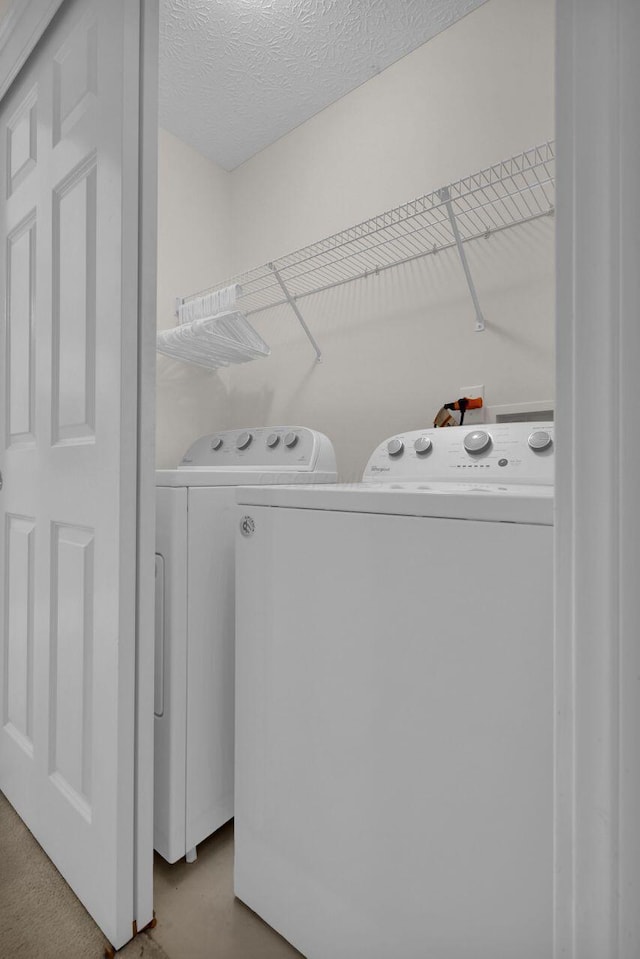 clothes washing area featuring a textured ceiling, laundry area, and washer and clothes dryer