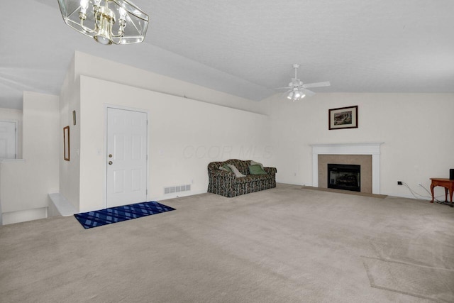 living area with visible vents, a fireplace with flush hearth, vaulted ceiling, carpet flooring, and ceiling fan with notable chandelier