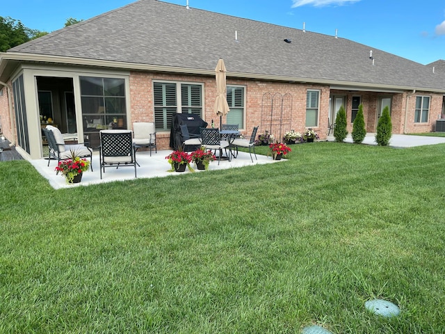 rear view of property with brick siding, a patio area, a shingled roof, and a lawn