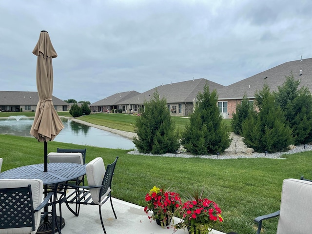 view of property's community featuring a lawn, outdoor dining area, a patio, and a water view