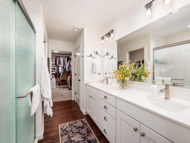 full bath featuring a walk in closet, double vanity, a stall shower, wood finished floors, and a sink