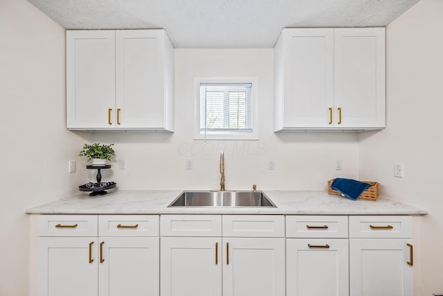 kitchen with a sink, light stone countertops, and white cabinets