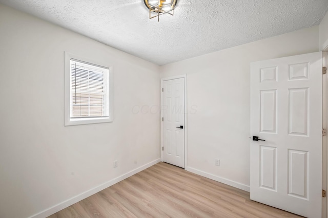 spare room featuring light wood-style flooring, baseboards, and a textured ceiling