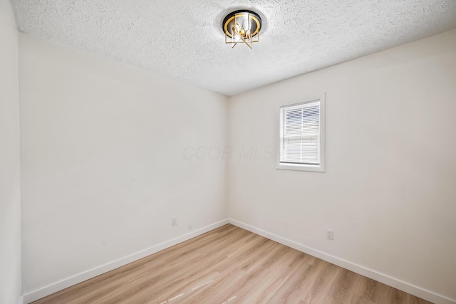 empty room featuring light wood finished floors, baseboards, and a textured ceiling