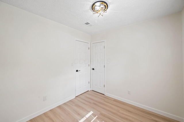 unfurnished room featuring light wood-type flooring, baseboards, visible vents, and a textured ceiling