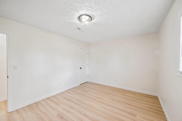 spare room with baseboards, a textured ceiling, and light wood finished floors