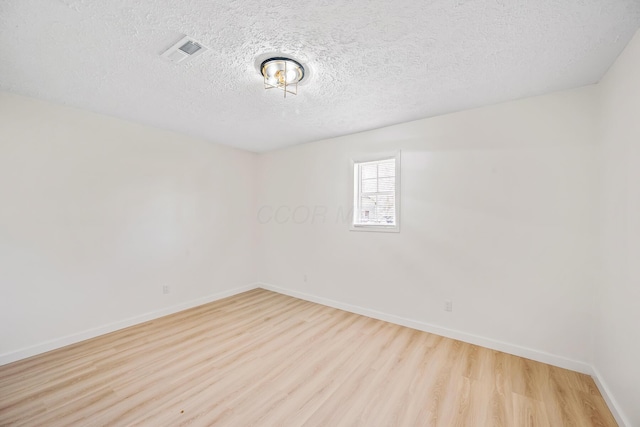 unfurnished room with a textured ceiling, wood finished floors, visible vents, and baseboards