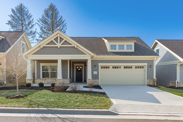 craftsman house with a front lawn, driveway, stone siding, an attached garage, and a shingled roof