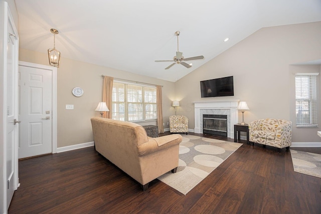 living area with wood finished floors, baseboards, a premium fireplace, vaulted ceiling, and ceiling fan with notable chandelier