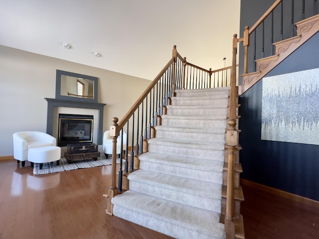 stairs with baseboards, wood finished floors, and a glass covered fireplace