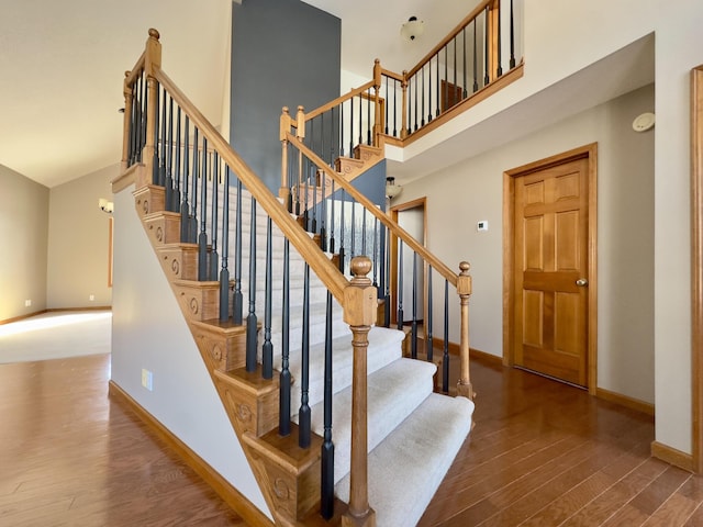 stairs featuring a towering ceiling, baseboards, and wood finished floors