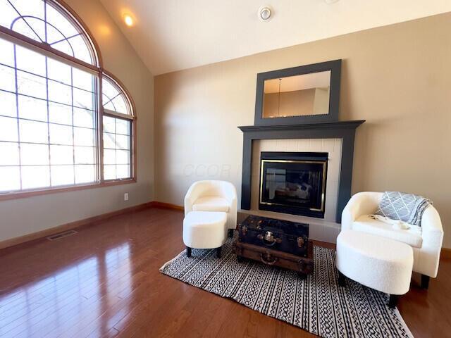 living area featuring baseboards, visible vents, wood finished floors, vaulted ceiling, and a fireplace