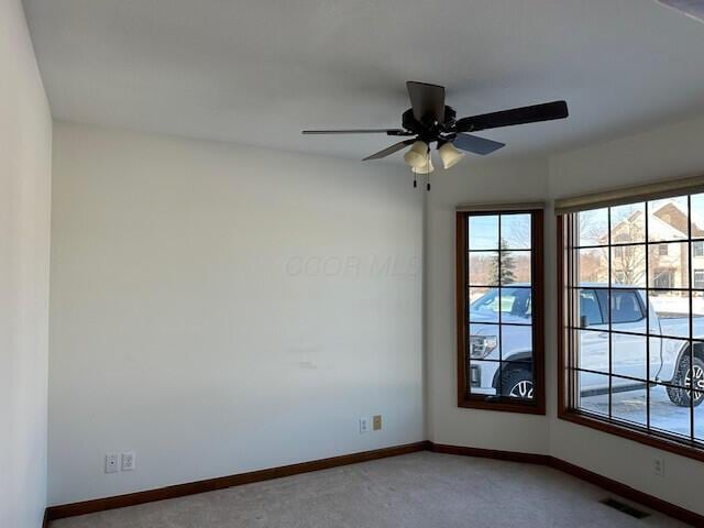 empty room featuring a ceiling fan, visible vents, light carpet, and baseboards