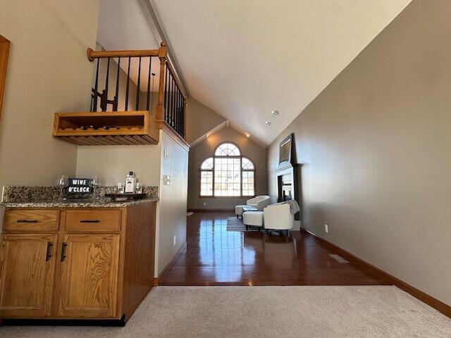 bar featuring carpet, a fireplace, high vaulted ceiling, baseboards, and stairs