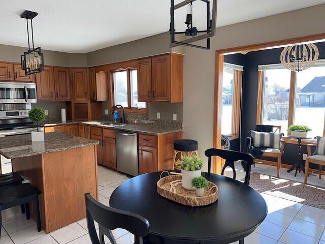 kitchen featuring brown cabinets, dark stone countertops, a center island, stainless steel appliances, and a sink