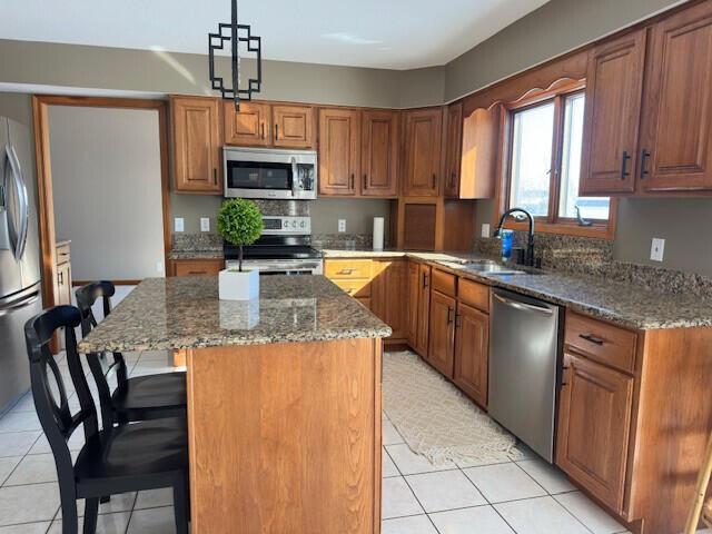 kitchen with stainless steel appliances, dark stone countertops, a sink, and a center island