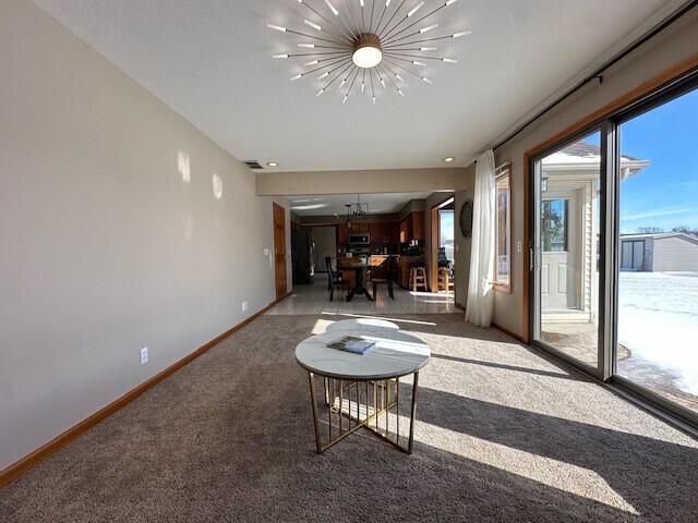 unfurnished living room featuring a chandelier, carpet, visible vents, and baseboards