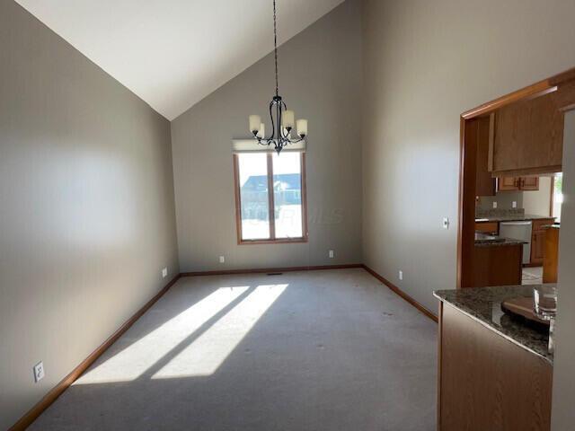 unfurnished dining area featuring light carpet, high vaulted ceiling, baseboards, and a notable chandelier