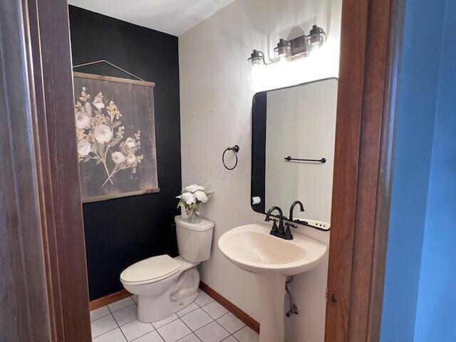 half bath featuring baseboards, toilet, and tile patterned floors