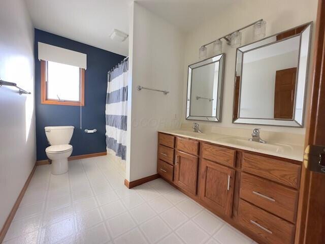 bathroom with toilet, double vanity, baseboards, and a sink