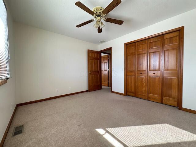 unfurnished bedroom featuring light carpet, baseboards, visible vents, ceiling fan, and a closet