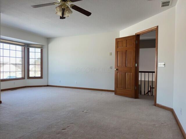 carpeted empty room with a ceiling fan, visible vents, and baseboards