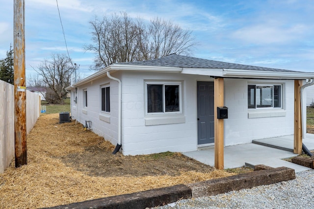 bungalow-style house with a shingled roof, fence, concrete block siding, and cooling unit