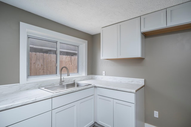 kitchen with light stone counters, white cabinets, a sink, and a textured ceiling