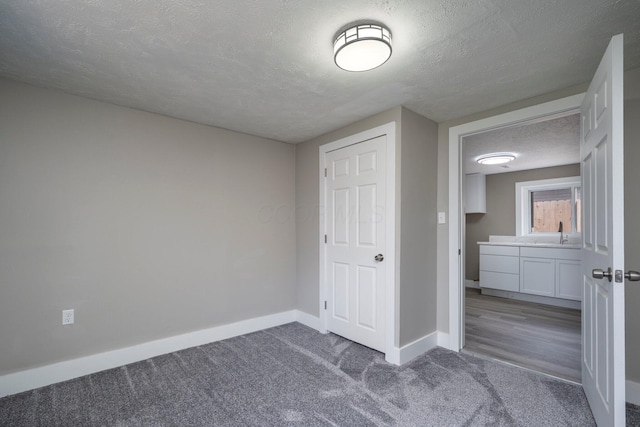 unfurnished bedroom with carpet floors, a sink, baseboards, and a textured ceiling