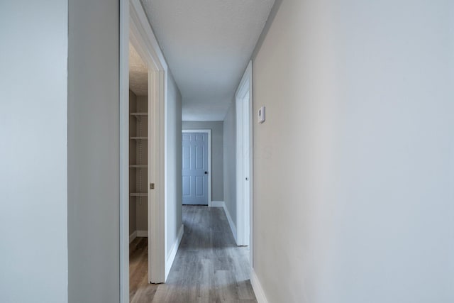 hall with light wood-type flooring, a textured ceiling, and baseboards