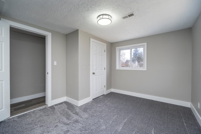 unfurnished bedroom with a textured ceiling, dark colored carpet, visible vents, and baseboards