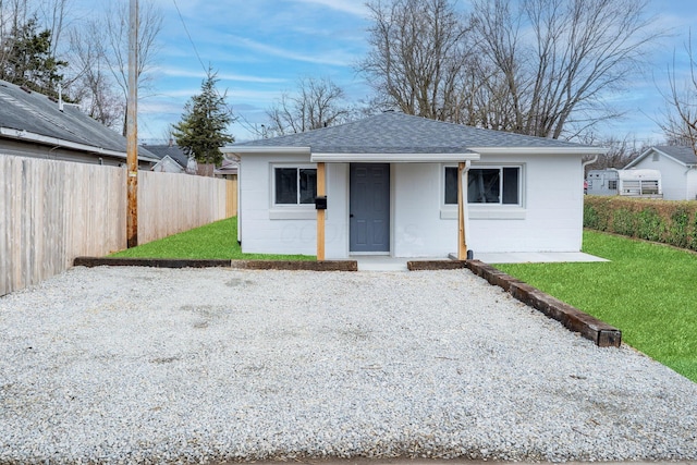 view of front of home featuring roof with shingles, a front yard, concrete block siding, and fence