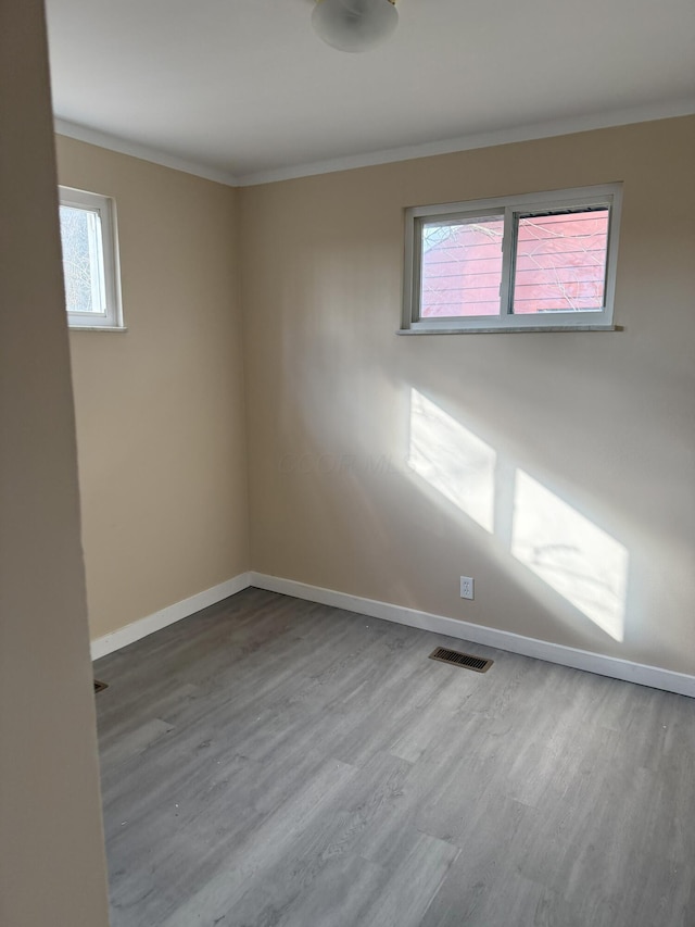 empty room with crown molding, visible vents, baseboards, and wood finished floors