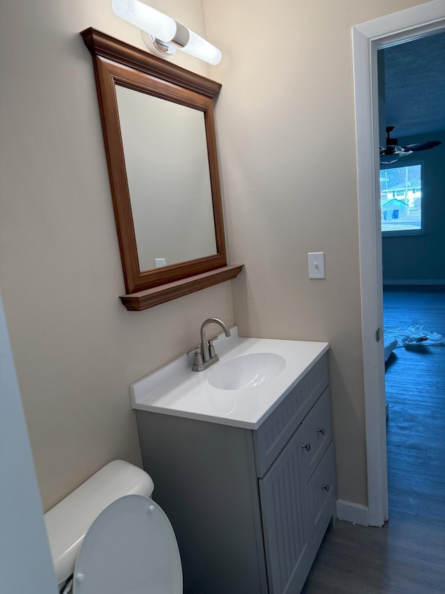 bathroom with baseboards, toilet, ceiling fan, wood finished floors, and vanity