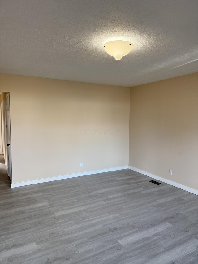 empty room with a textured ceiling, wood finished floors, visible vents, and baseboards