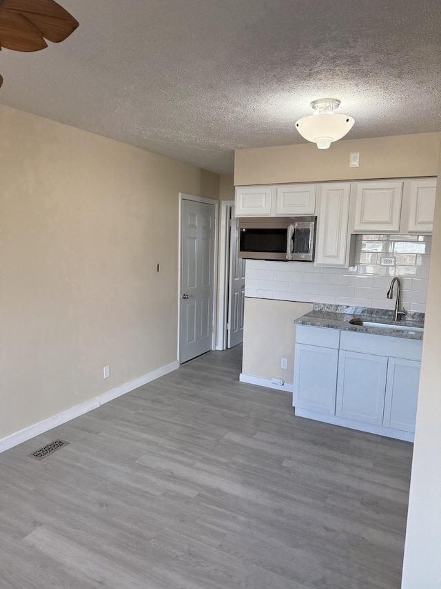 kitchen with white cabinets, stainless steel microwave, wood finished floors, a sink, and backsplash