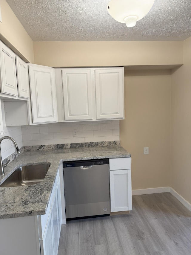 kitchen featuring light wood finished floors, decorative backsplash, stainless steel dishwasher, white cabinets, and a sink