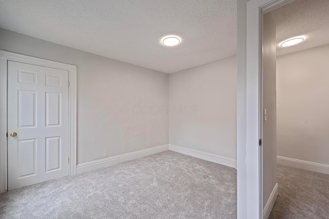 unfurnished room with a textured ceiling, carpet flooring, and baseboards