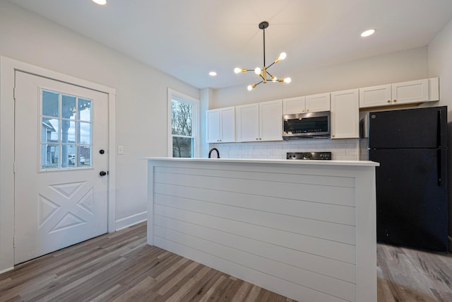 kitchen with wood finished floors, white cabinetry, freestanding refrigerator, tasteful backsplash, and stainless steel microwave