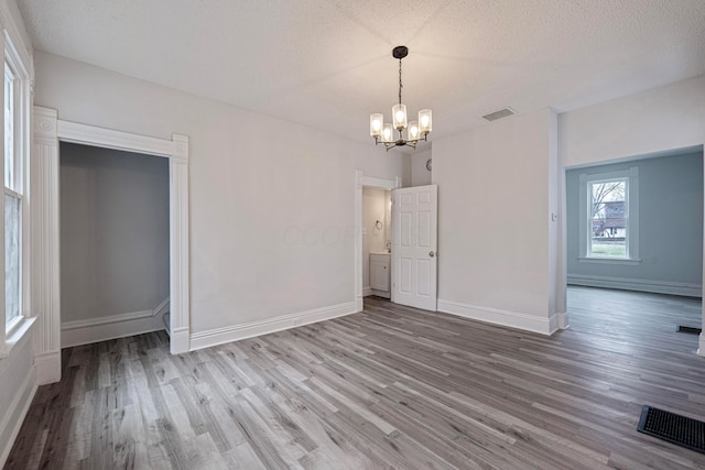 unfurnished dining area featuring visible vents, a notable chandelier, a textured ceiling, and wood finished floors