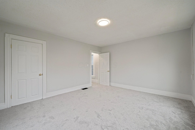 spare room featuring a textured ceiling, carpet, visible vents, and baseboards