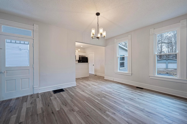 unfurnished dining area featuring an inviting chandelier, visible vents, a wealth of natural light, and wood finished floors