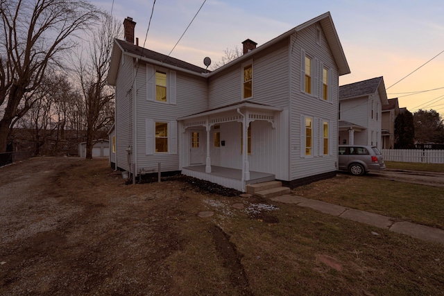 view of front of home featuring covered porch, a chimney, fence, and a lawn